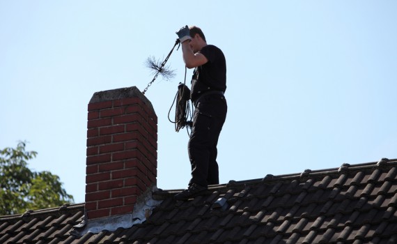 Chimney sweep inserting a coarse wire brush into the flue of a chimney while standing on top of the roof